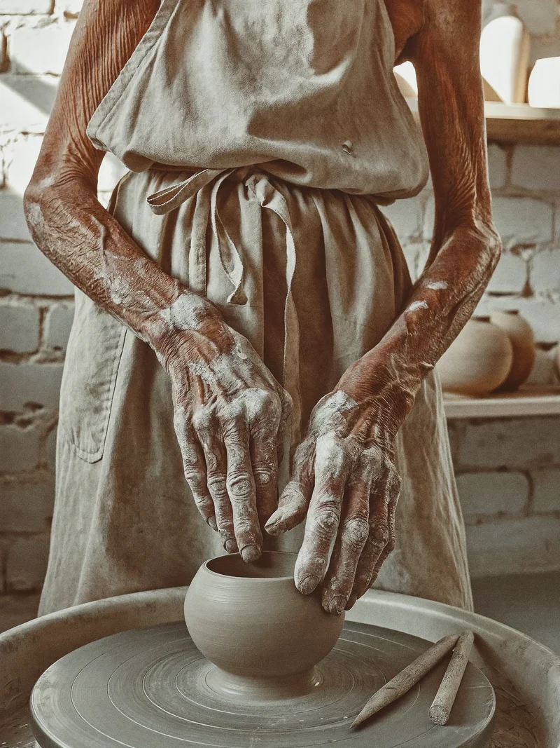 Mani anziane che modellano una piccola ciotola d'argilla al tornio in uno studio luminoso.